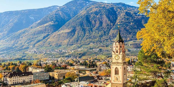 Meran im goldenen Herbst – Blick auf Altstadt und Bergwelt Herbstlicher Blick über die Altstadt von Meran mit Stadtturm, bunten Bäumen und der umliegenden Berglandschaft Südtirols im goldenen Herbstlicht.